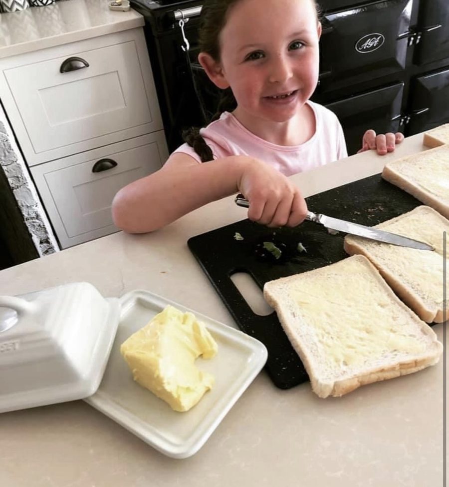 A very young Elsie smiling as she butters slices of bread